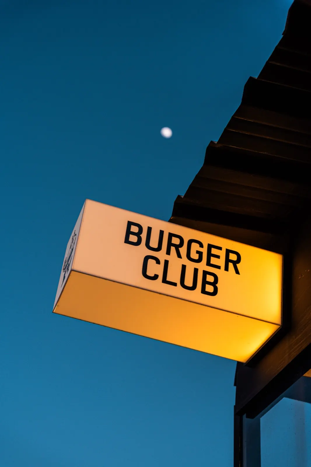 Cartel Burger Club iluminado al anochecer con la luna de fondo