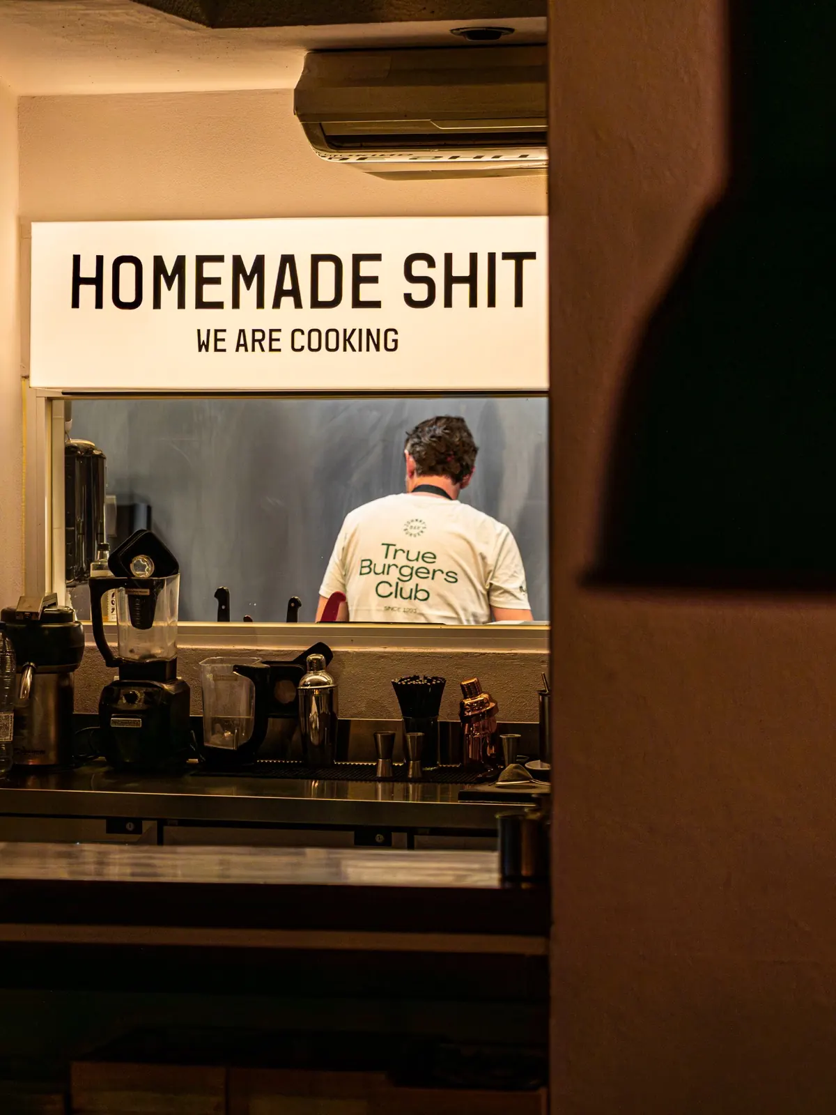 Cocina de Johnny's vista desde la ventanilla Homemade Shit con cocinero de espaldas